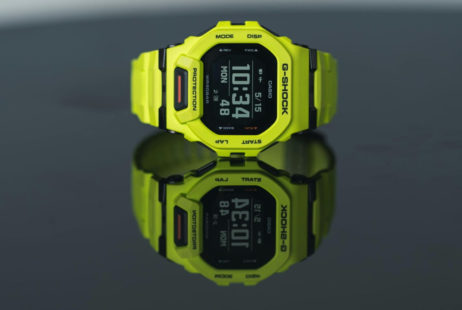 A vibrant yellow digital watch displayed on a glossy black surface, showing time clearly.